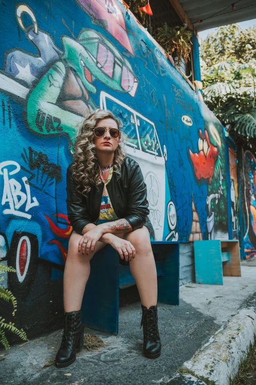 a girl sitting in front of a large blue graffiti covered building