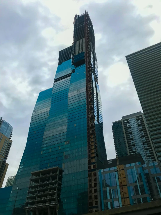 tall skyscrs and cranes near each other against cloudy sky