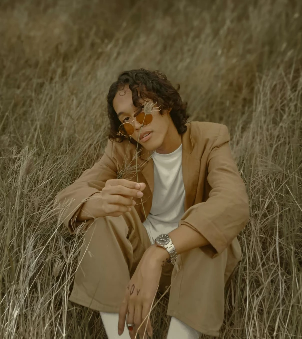 a person wearing a tan jacket and sunglasses sitting in some tall grass