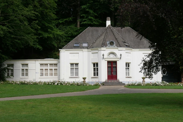 a large white building with red door sitting on the side of a green field