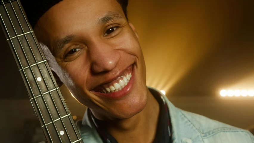 a man wearing a blue denim shirt holds up a guitar