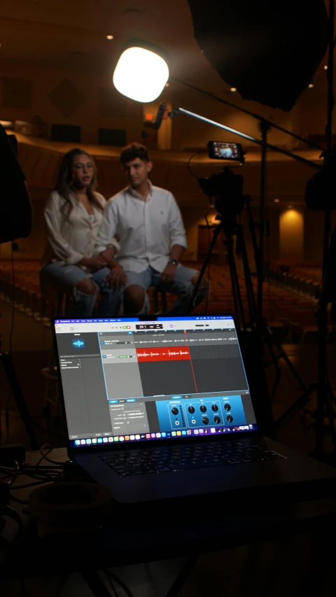 two people sitting behind a laptop computer in a dark room