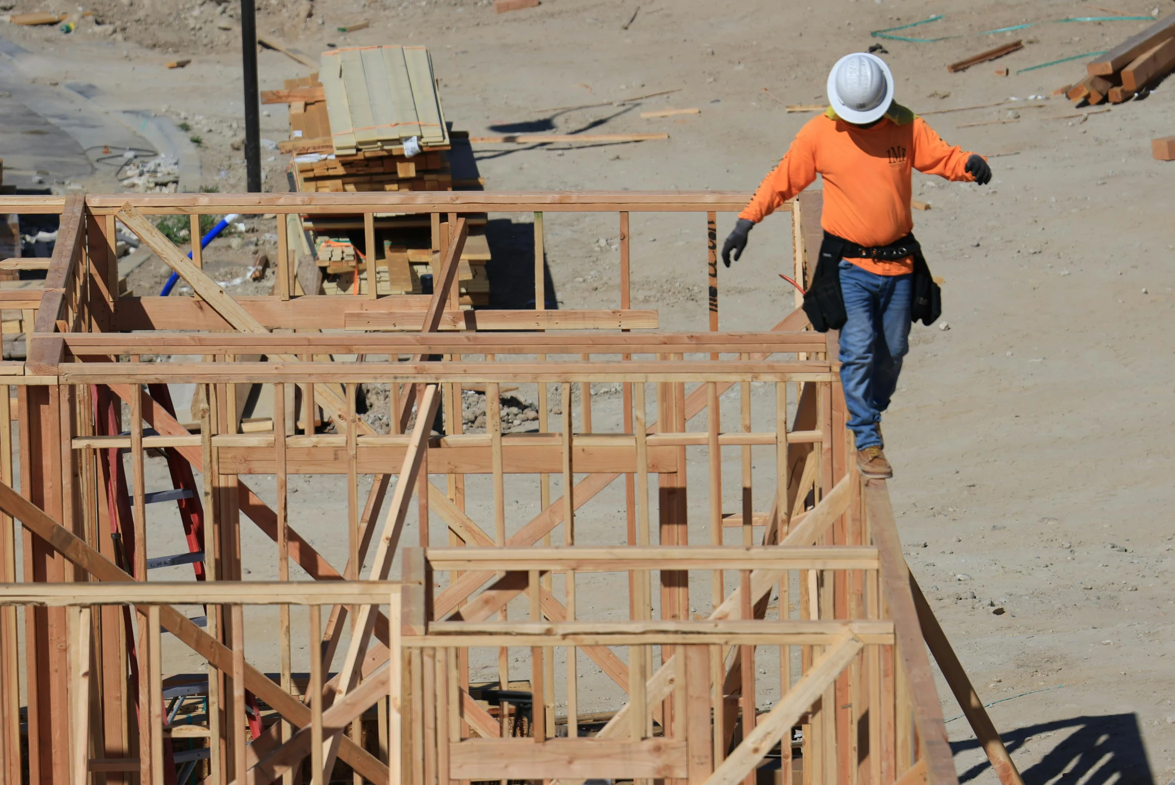 a man wearing an orange jacket walking around a house construction site