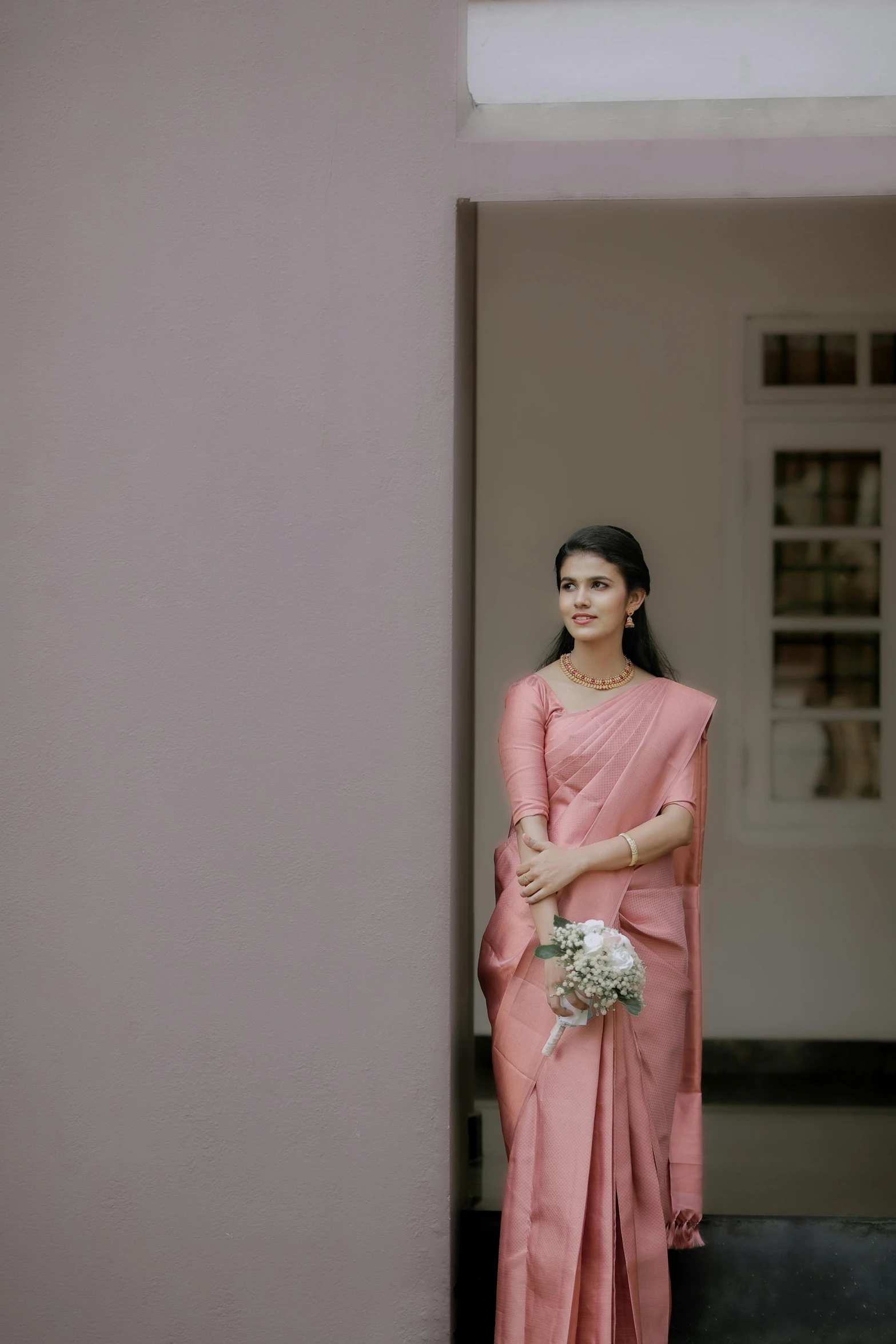 the woman is standing near a wall wearing pink dress