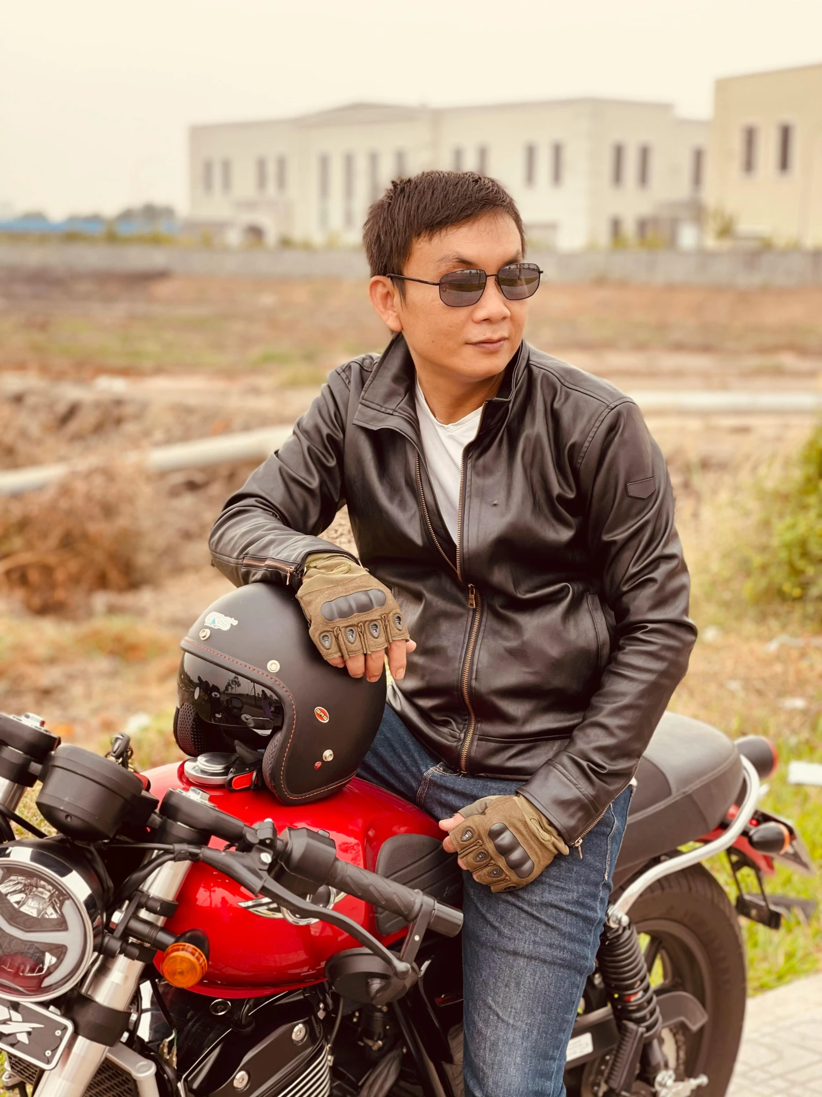 a man wearing a black leather jacket sitting on his red motorcycle