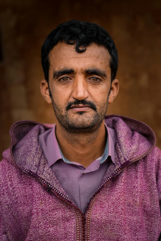 man with goatee in pink sweater standing in front of brown wall