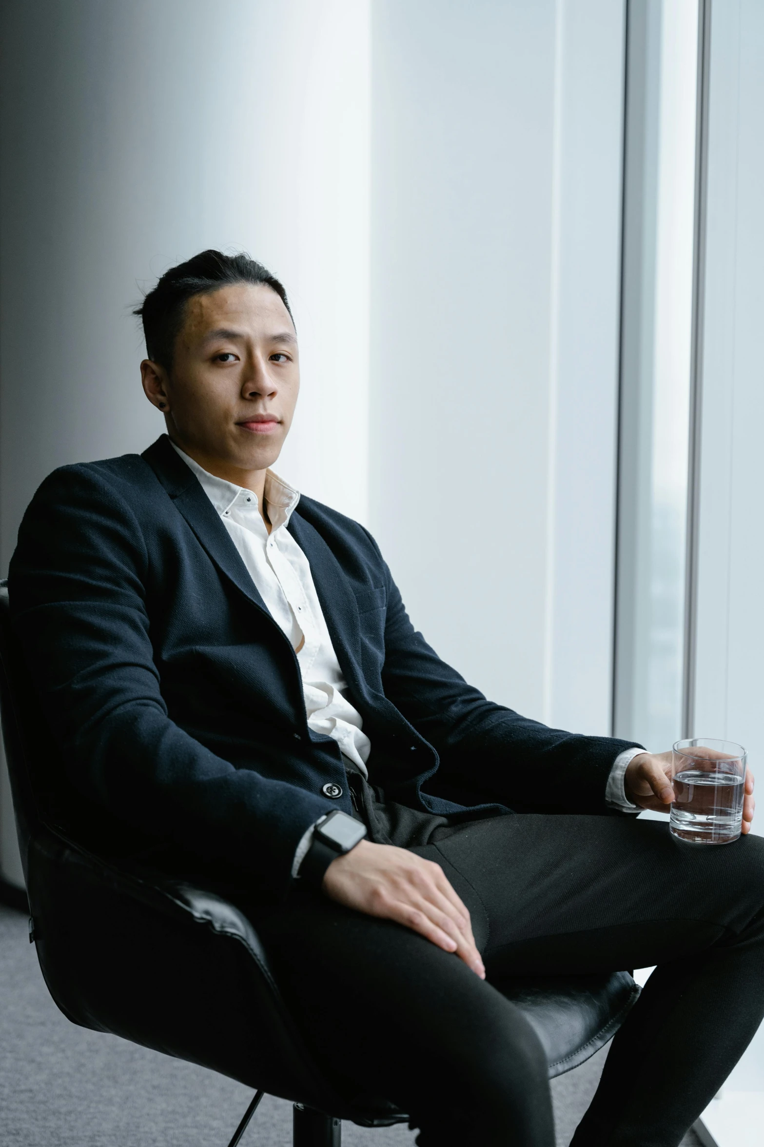 man sitting on a chair in the corner with his arms folded, in front of a glass