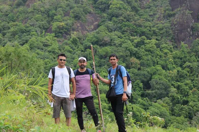 three men standing on top of a lush green forest