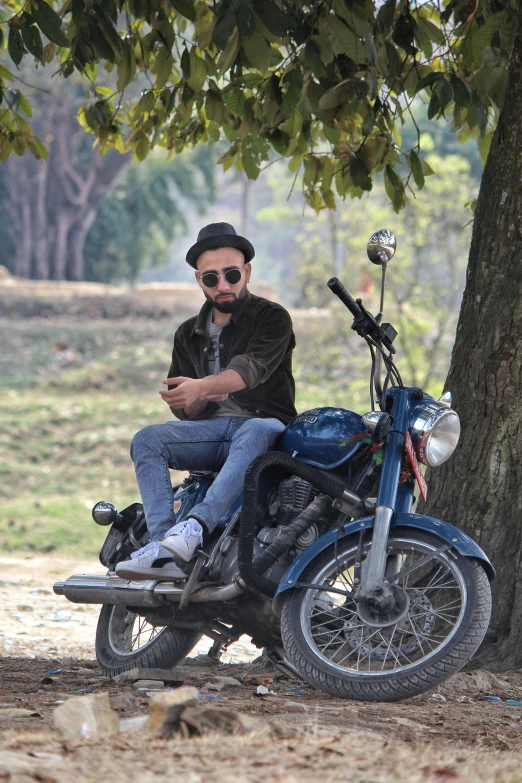 a man in black hat sitting on blue motorcycle