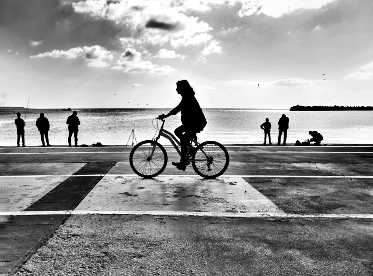 a woman riding her bike with other people standing around and looking out to sea