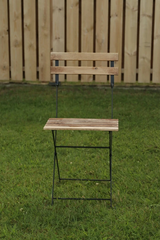 a wooden chair sits in the grass near a fence