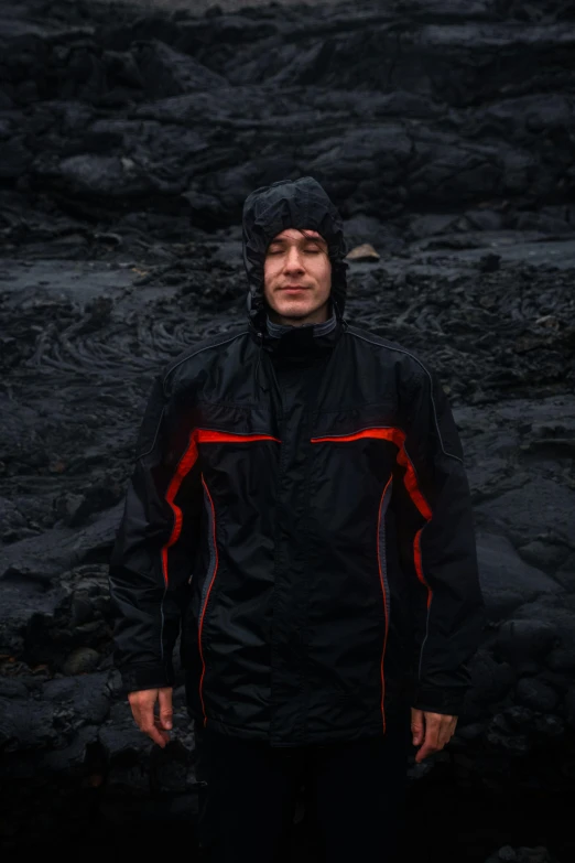 man wearing rain jacket standing in dark rocky area