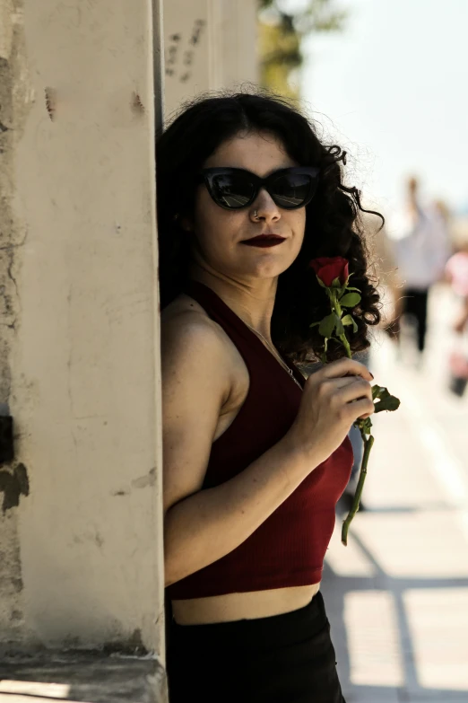 a women that is standing up against a wall with a rose