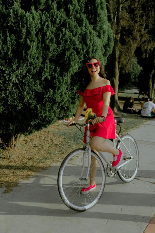 a woman in red dress on bicycle with trees and grass