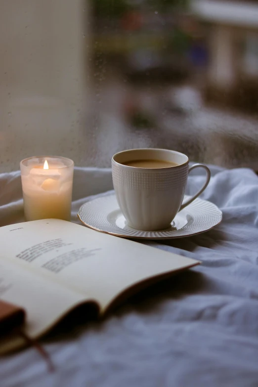 a book, candle and cup are setting on the bed