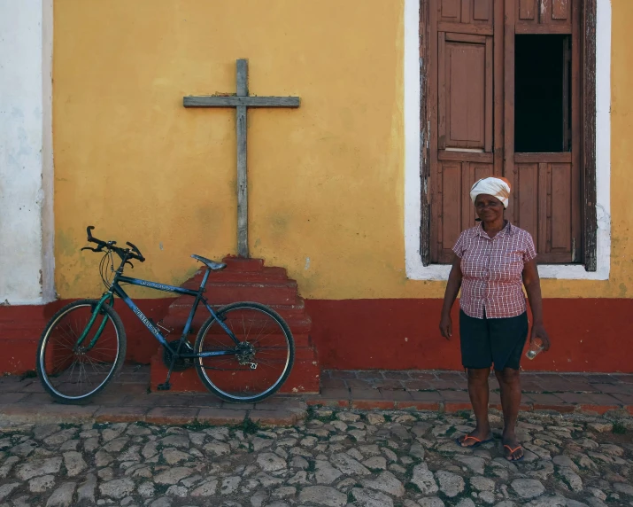 a woman in a bandana stands by a bicycle on the side walk