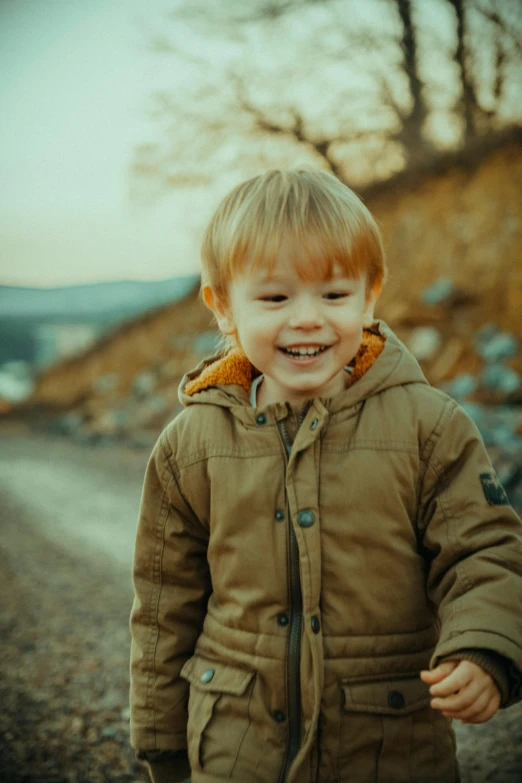 a small boy laughing while walking across a dirt road