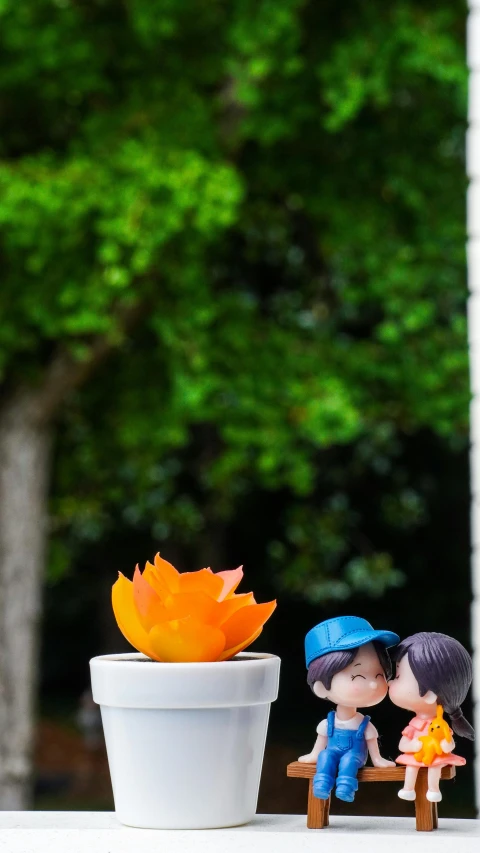 a little toy couple is sitting in front of a potted plant