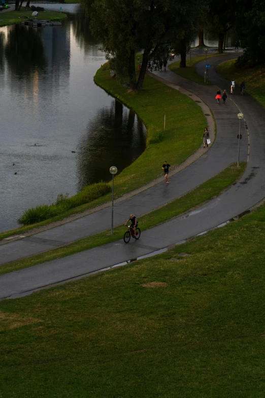 people riding bikes down the winding road by the water