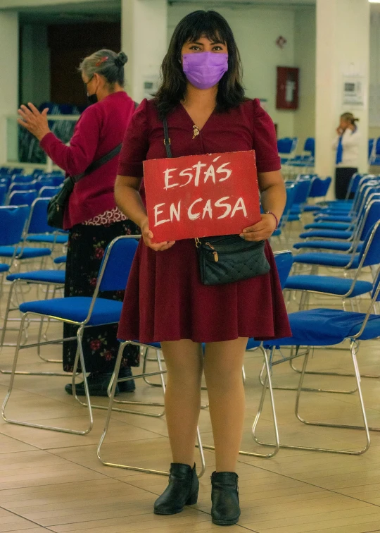 a woman wearing a mask holding up a sign that reads estas encasa