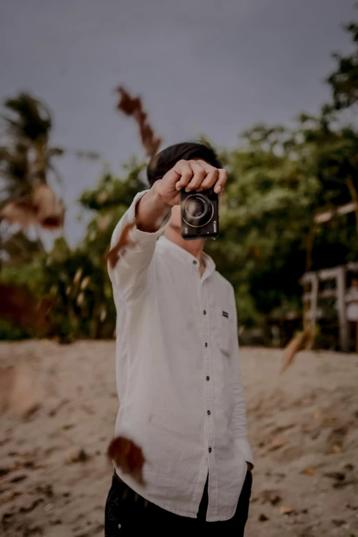a man standing on top of a sandy beach holding a camera up to the sky
