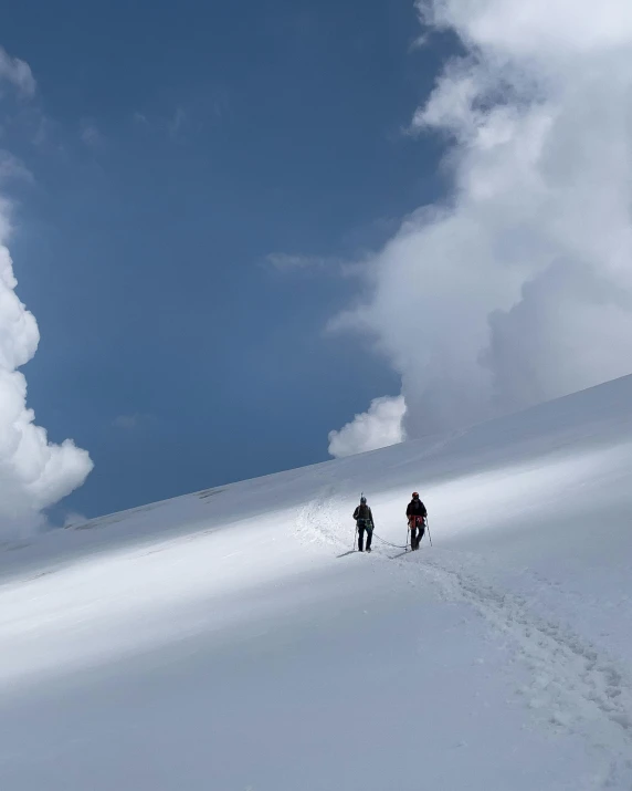 two people walking down a snowy hillside under a cloudy sky