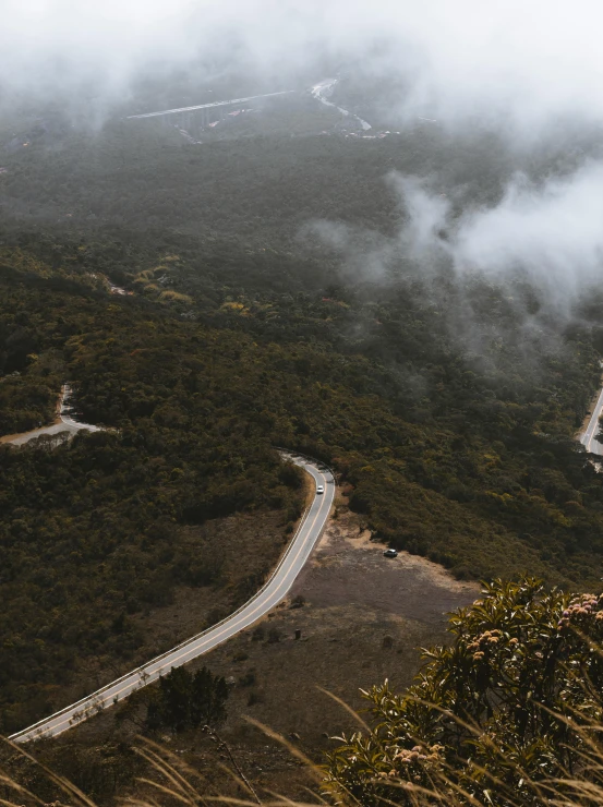 a mountain covered with low hanging clouds, and a road winding up a hill