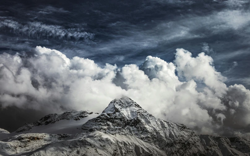 a mountain covered in snow and clouds on a cloudy day