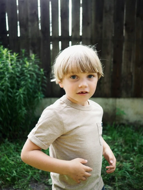 a boy with blond hair in a tan t - shirt