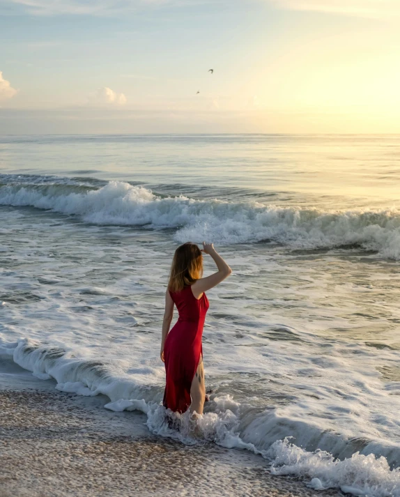 a woman in a red dress standing in the surf