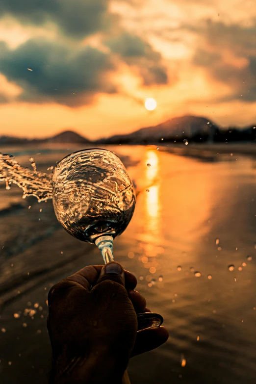 hand holding wine glass over water at sunset on beach