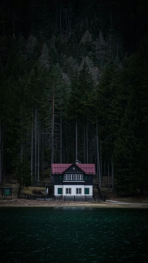 an old white house is near a lake in a forested area