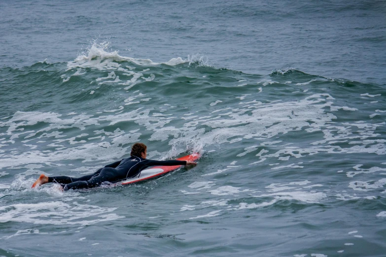 a person in a wet suit laying on a surfboard with their foot propped up on top of a wave