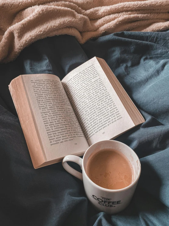 an open book on a blanket with a cup of coffee next to it