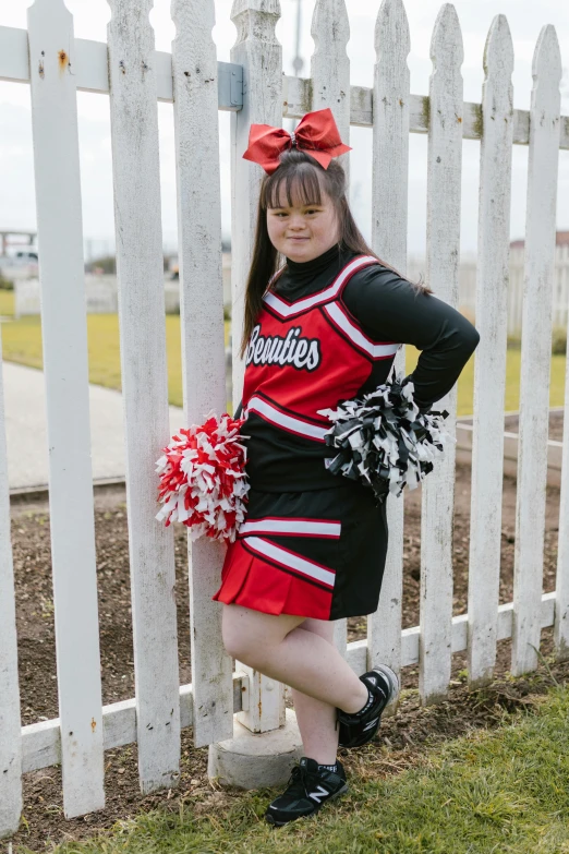 a woman in black and red cheer uniform leaning on a fence