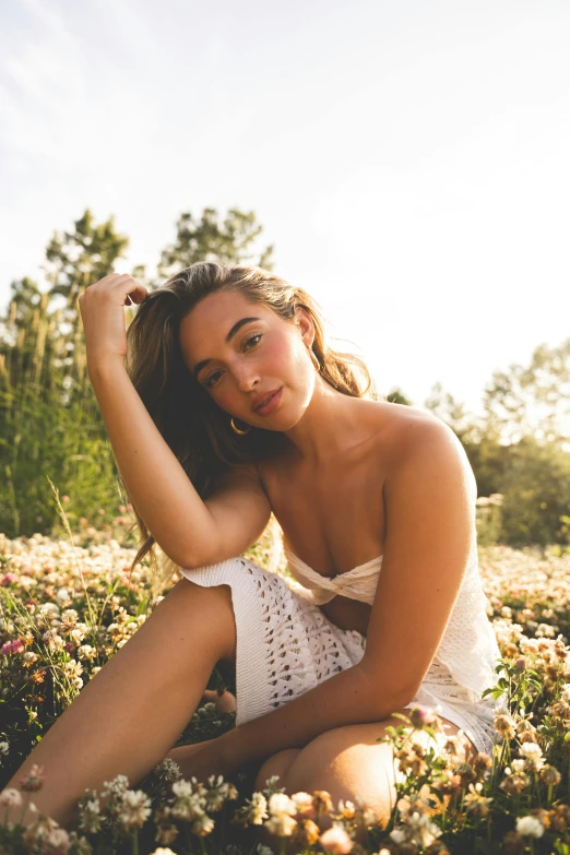 a woman sits in a field of flowers in a dress