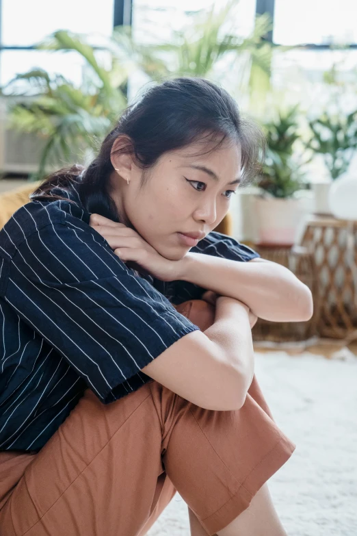 a young woman sitting on the floor with her hand on her chin