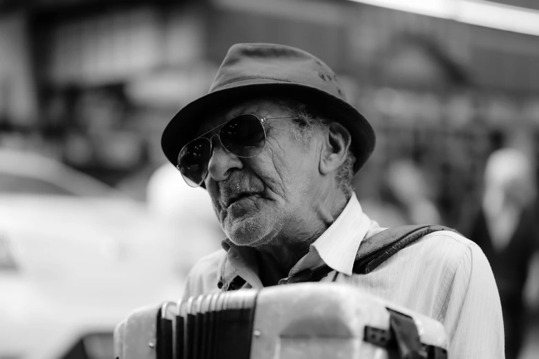 an elderly man with a hat and sunglasses plays a accordion