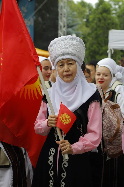 a woman in traditional clothing holding a red flag and two flags