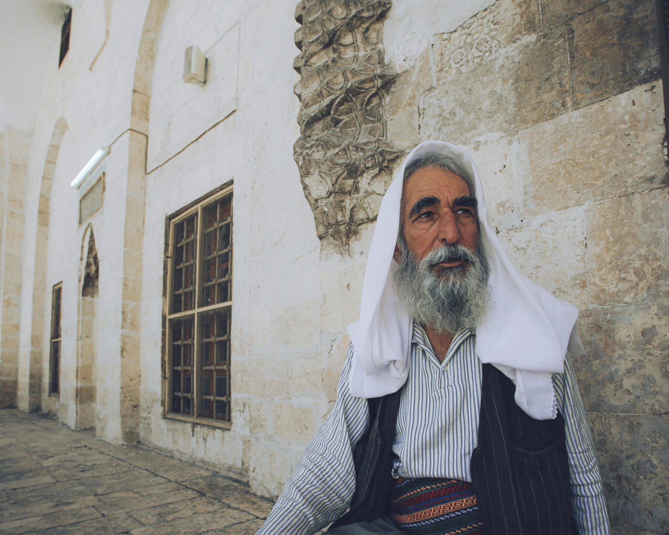 the old man has grey beard and white shirt