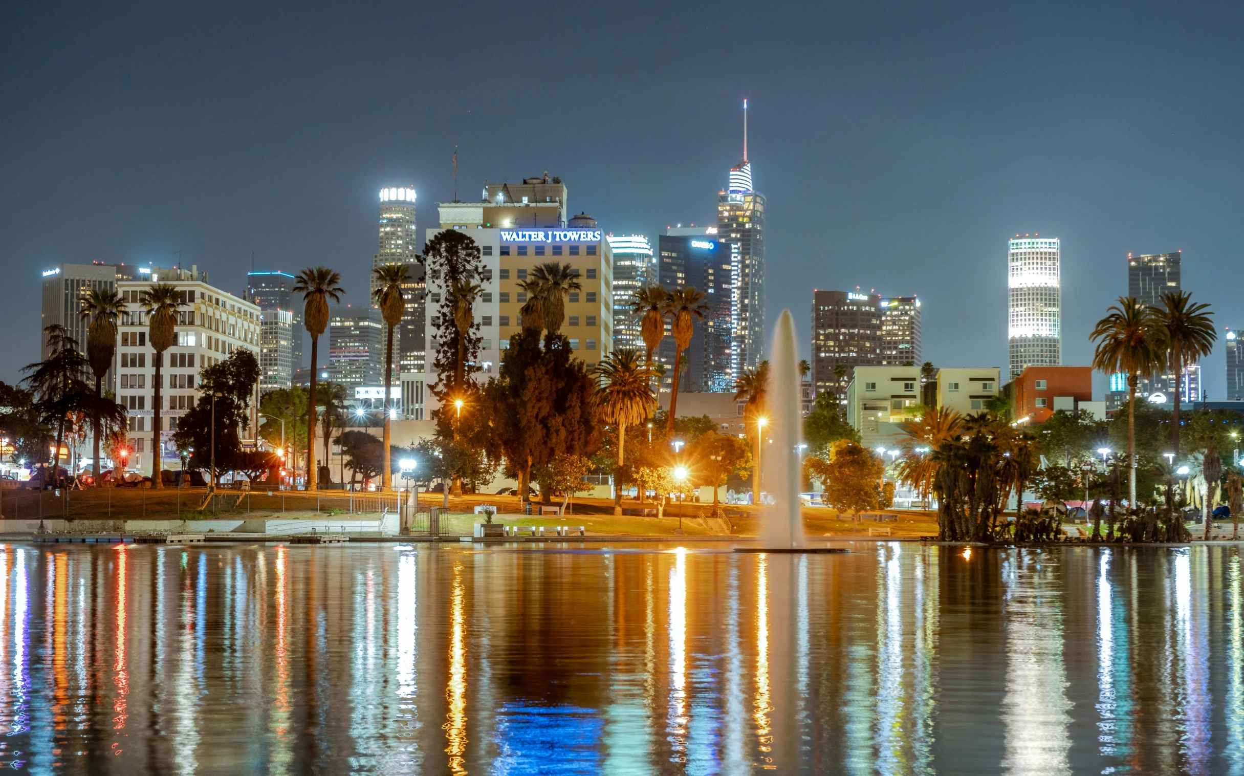 a skyline with buildings, trees and lights reflected in the water