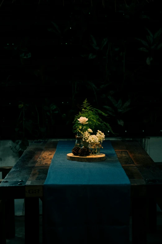 flowers are sitting on a long table with blue linen