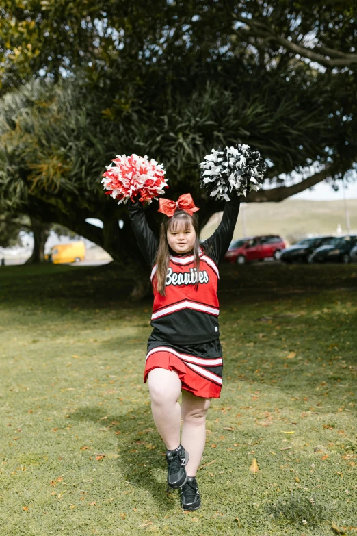 a girl in a cheerleader costume stands on a lawn and holds her arms up