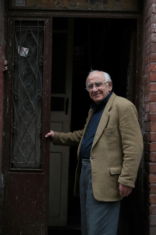 a man in glasses and jacket standing outside a doorway