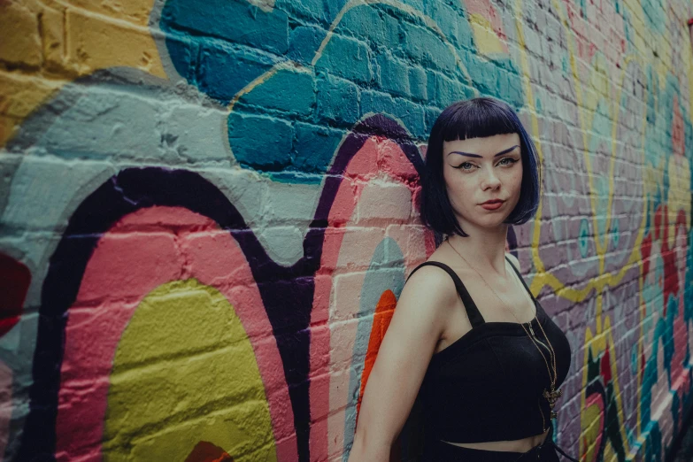 a girl standing near a painted brick wall