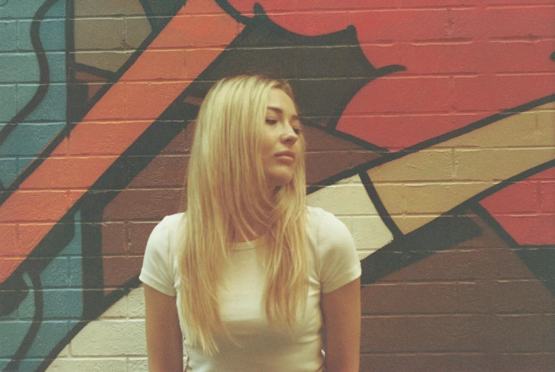 a blonde girl with long hair standing in front of graffiti