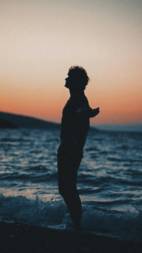 a man standing on a beach at sunset looking out to sea