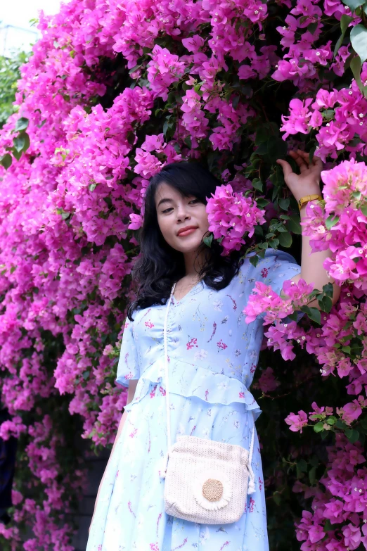 a lady posing for a po next to a bush of pink flowers