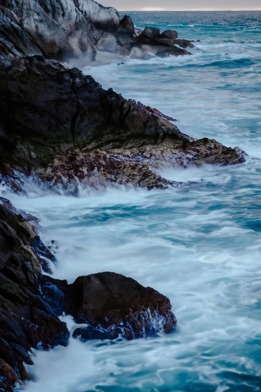 the ocean is blue and calm as waves crash on rocks