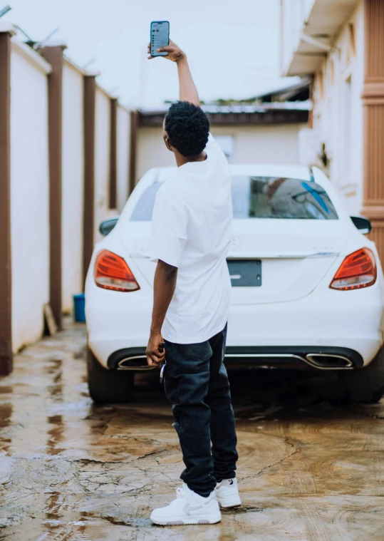 a man holding up a cell phone next to a car